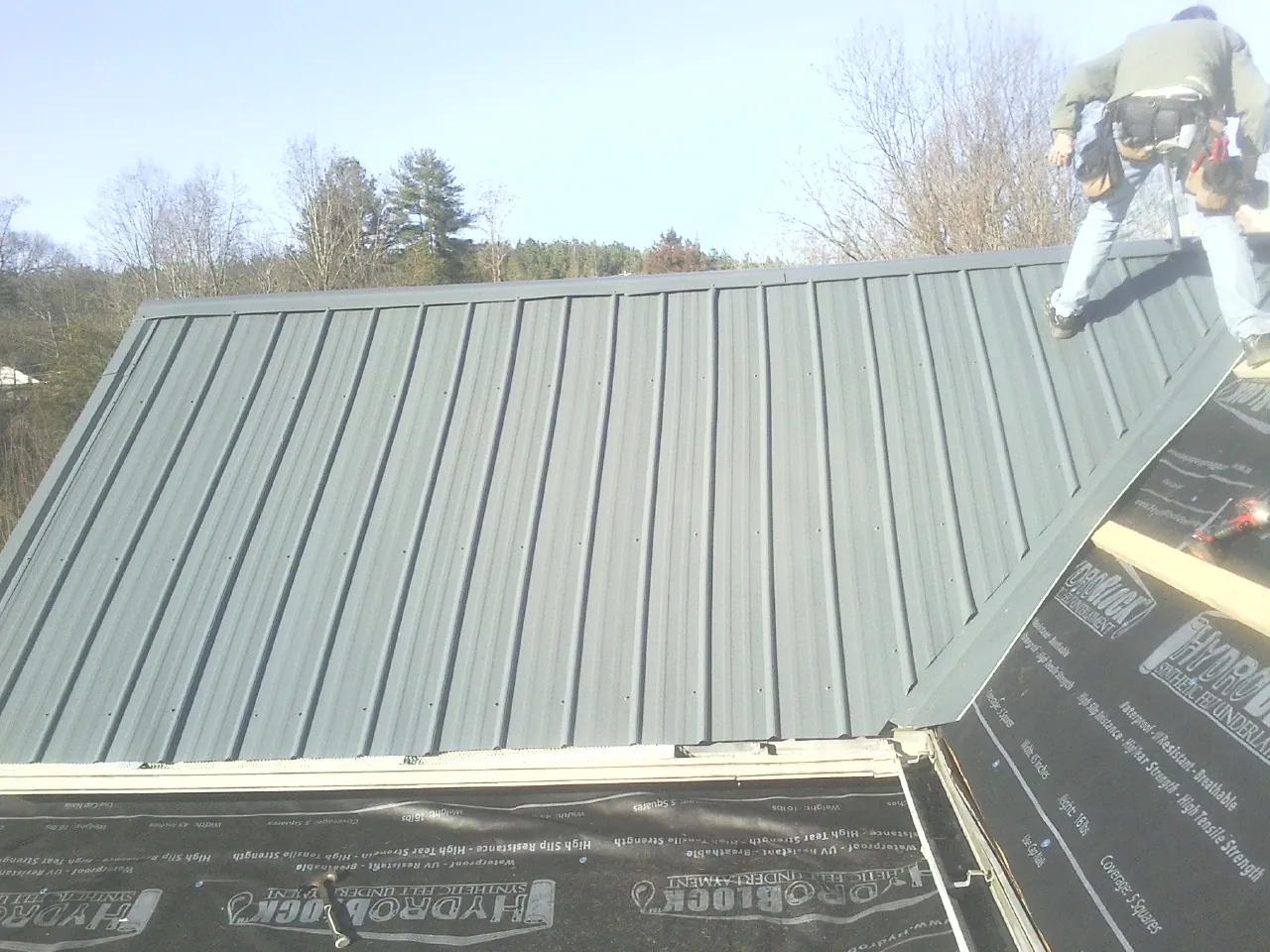 Crew installing dark green standing seam panels over synthetic underlayment in Blue Mounds