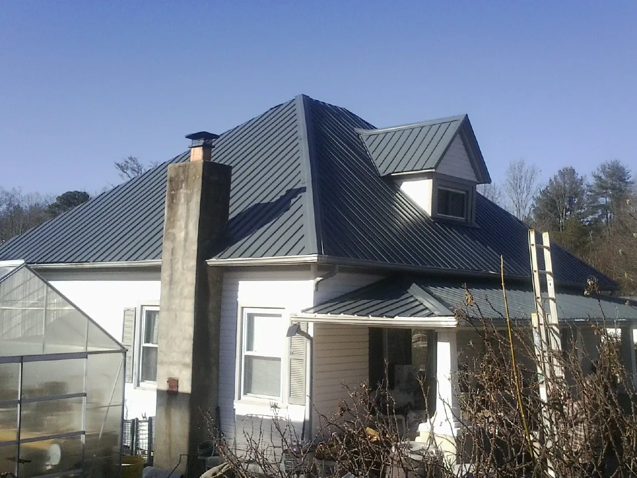 Dark blue standing seam metal roof on a white farmhouse with dormer — Slate & Tile Roof Repair by Roofing Brothers in Blue Mounds