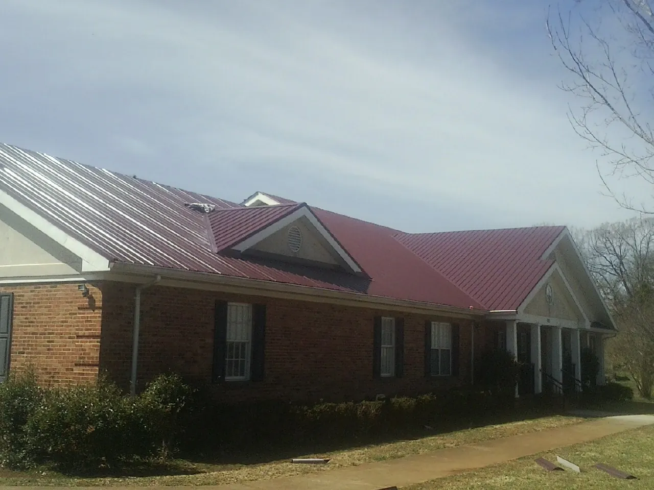 Red metal roof with gabled entries on a long brick building, from a Hail Damage Roof Repair job in Blue Mounds