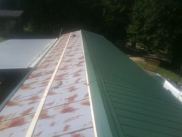 Old rusted panels beside newly installed green metal roofing — Wind Damage Roof Repair by Roofing Brothers in Blue Mounds