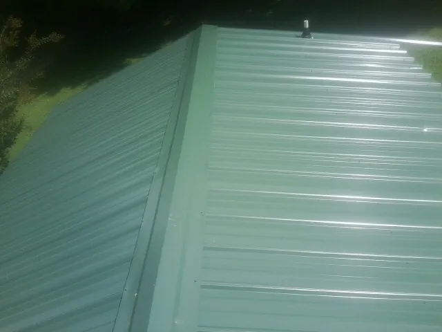 New green metal panels meeting at the ridge of a roof — Flat Roof Repair work by our crew in Blue Mounds