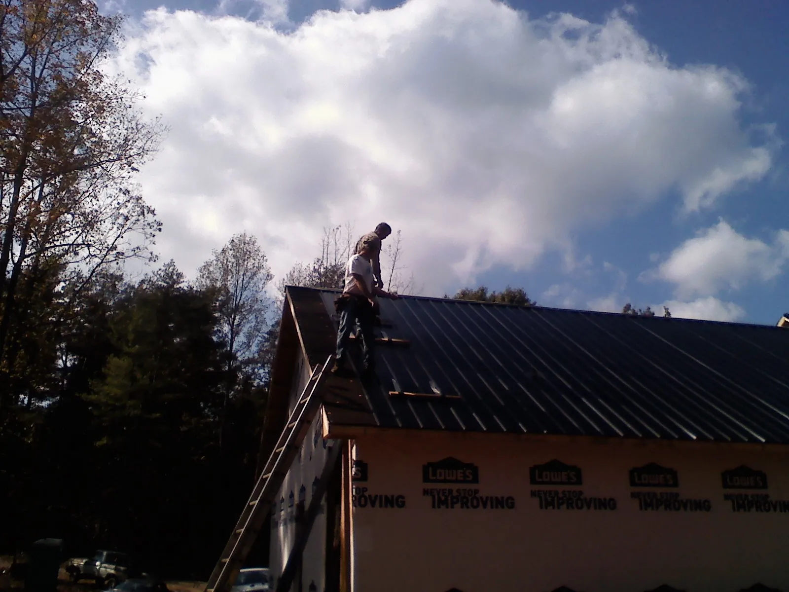 Roofer fastening dark metal panels high against a cloudy sky, from a Roof Inspection job in Blue Mounds