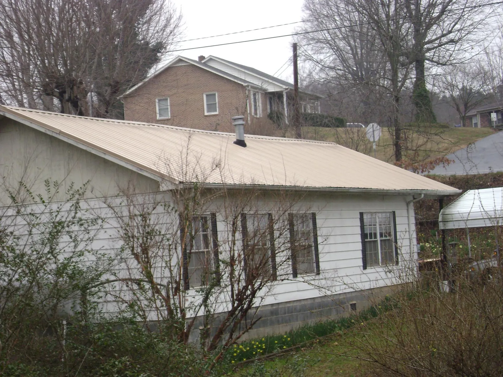 Tan metal roof on a white sided house set into a hillside — Commercial Roofing by Roofing Brothers in Blue Mounds