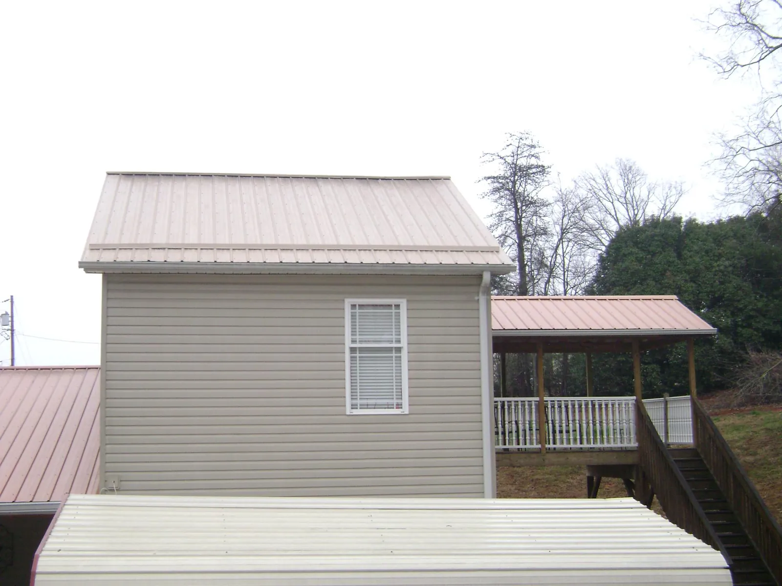 Tan metal roofs on a two story addition and attached porch, from a Roof Replacement job in Blue Mounds